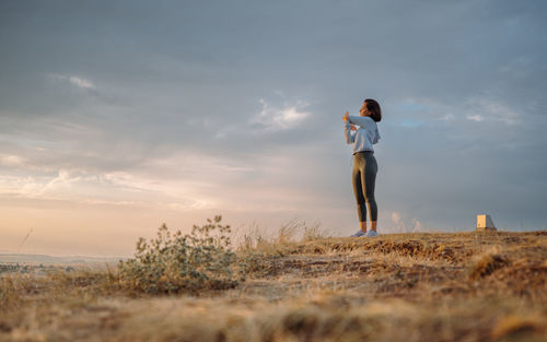 Rear view of woman standing on rock against sky during sunset