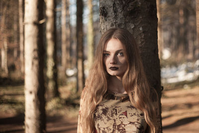 Portrait of young woman standing against trees