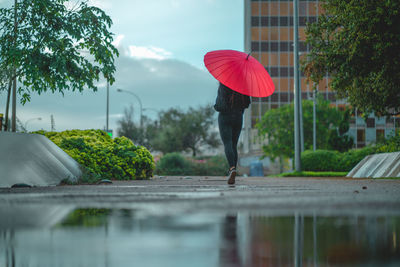 Woman with red umbrella walking behind a puddle in palma, spain