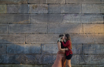 Portrait of two girls standing against stone wall