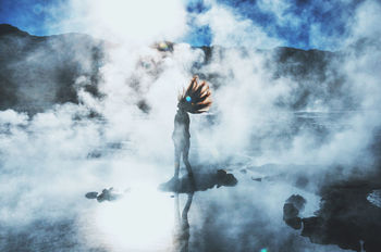 Silhouette young woman with tousled hair standing in lake during foggy weather