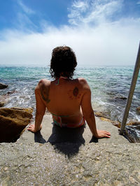 Rear view of man sitting on beach against sky