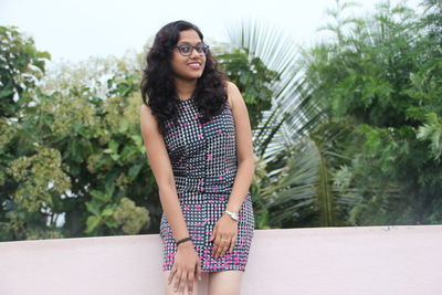 Portrait of smiling young woman standing against trees