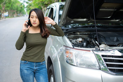 Angry asian woman and using mobile phone calling for assistance after a car breakdown on street. 