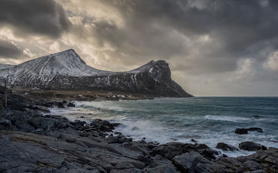 Scenic view of sea by mountain against sky