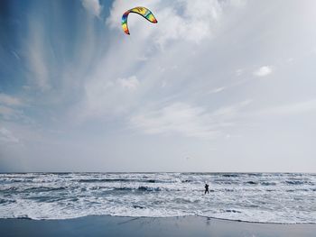 Person paragliding over sea against sky