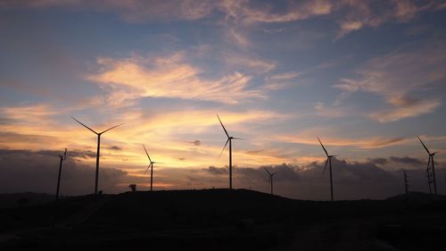 Silhouette wind turbines on land against cloudy sky at sunset
