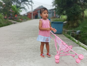 Cute girl holding baby stroller standing on footpath