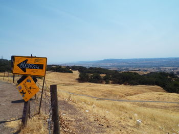 Road sign on field against sky