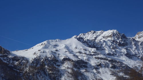 Low angle view of snowcapped mountains against clear blue sky