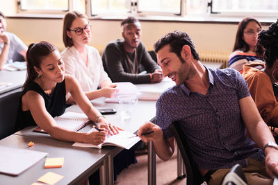 Multi-ethnic friends discussing over book in classroom