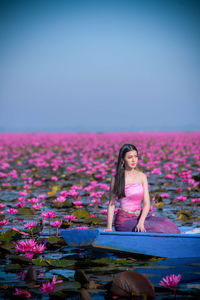 Woman sitting in boat amidst pink flowers on lake