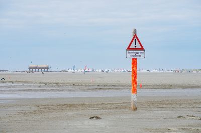 Road sign on beach against sky