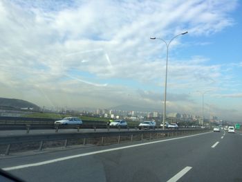 Cars on road against cloudy sky