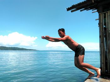 Shirtless man diving into sea against blue sky