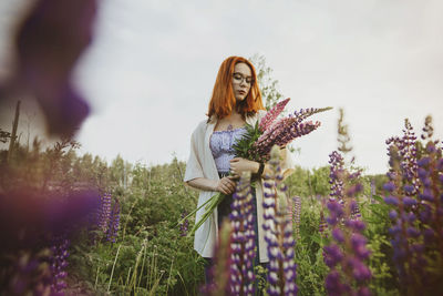 Teenage girl standing with lupin flowers under sky