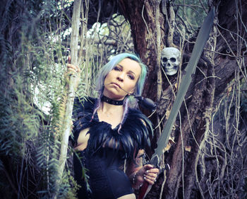 Portrait of woman model holding sword against trees