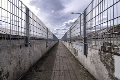 Empty footpath amidst walls against sky