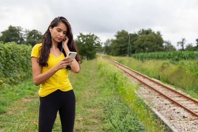 Serious young ethnic lady listening to song and using smartphone in nature