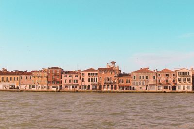 Buildings by sea against clear blue sky