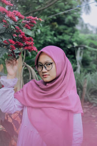 Portrait of young woman standing by pink flowers