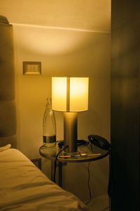 Illuminated electric lamp on table by wall at home