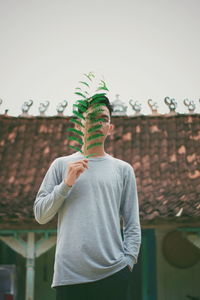 Portrait of young man holding leaf while standing outdoors