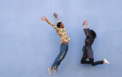 Black couple jumping outdoor with blue wall in background - main focus on man face