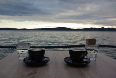 Close-up of coffee cup on table against sea during sunset