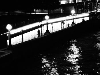 People on illuminated bridge over river at night