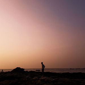 Silhouette man on beach against clear sky during sunset