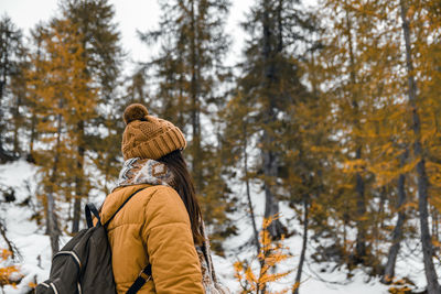 Rear view of young woman hiking on snowy path surrounded by yellow larch trees