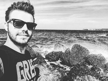 Portrait of young man wearing sunglasses at beach against sky