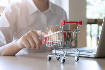 Midsection of man touching miniature shopping cart by laptop on table