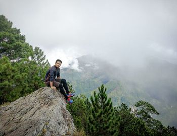 Portrait of man sitting on rock against sky