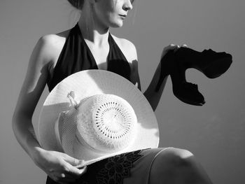 Midsection of woman holding hat and shoes against gray background