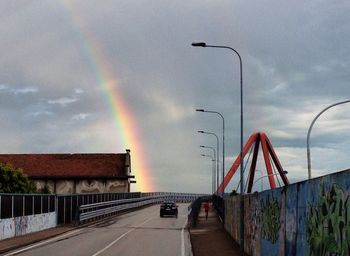 Rainbow over road against cloudy sky