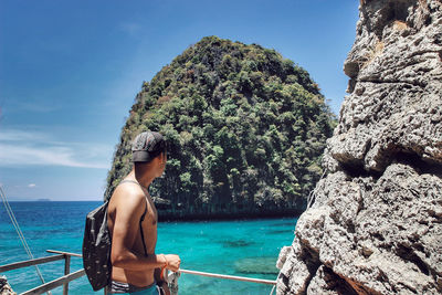 Side view of man standing against railing looking at view of sea