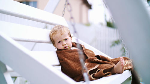 A little one-year-old girl, wrapped in a towel, with a dirty face, lonely sitting on a swing in the