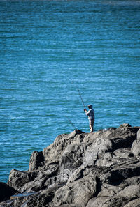 Man fishing on rock by sea