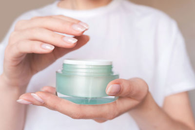 Female hands with natural pink manicure holding a transparent cream jar. woman holds beauty product