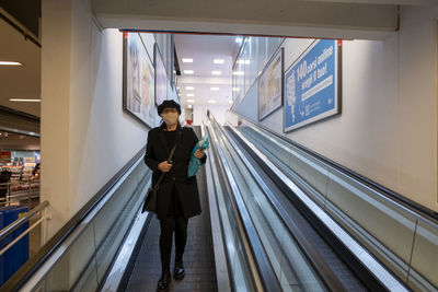Woman wearing mask standing on escalator