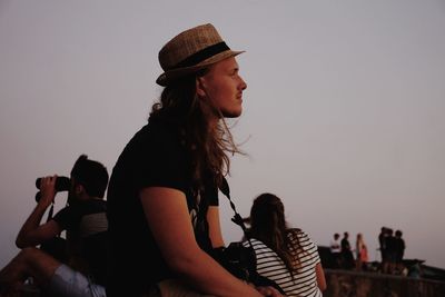 Side view of young woman sitting in park against sky