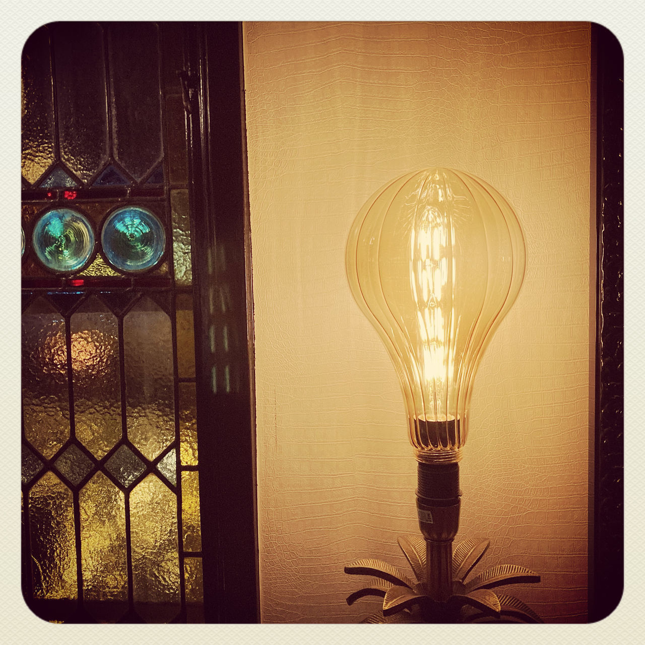 CLOSE-UP OF ILLUMINATED LIGHT BULB HANGING AGAINST WALL