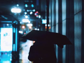 Silhouette person holding umbrella on street during rainy season at night