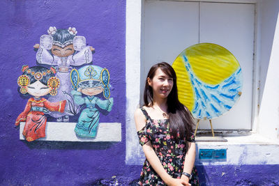 Portrait of smiling young woman standing against wall