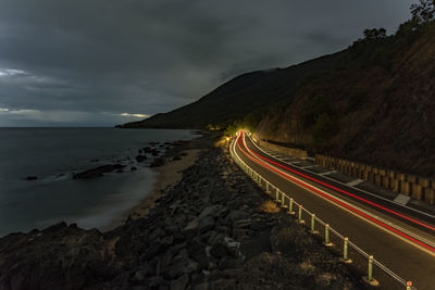 Light trails on road by mountain against sky at night