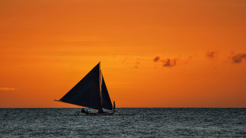 Sailboat on sea against orange sky