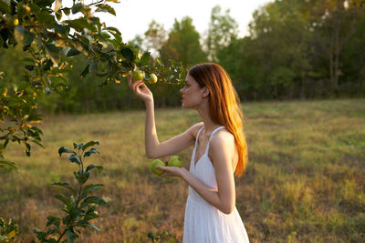 Side view of woman standing by tree against plants