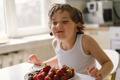 Cute beautiful little boy eating fresh cherry and strawberry.